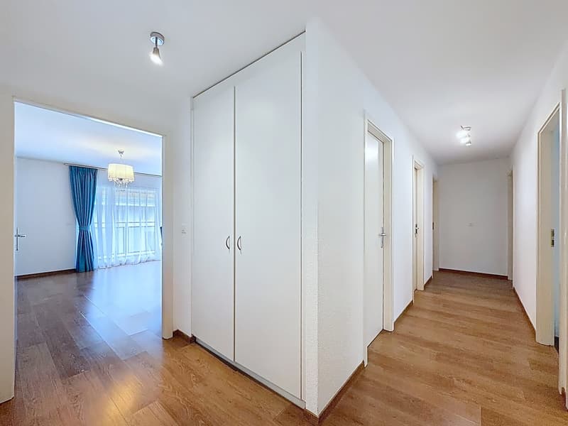 Empty hallway with wooden floor, white walls, large wardrobe, and two chandeliers