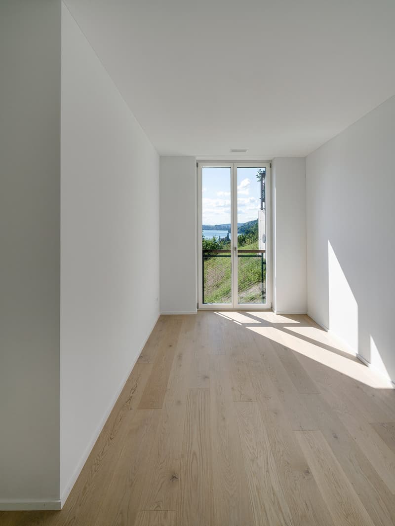 Spacious room with large windows offering a scenic view of the surrounding landscape. The room has white walls and light-colored hardwood flooring.