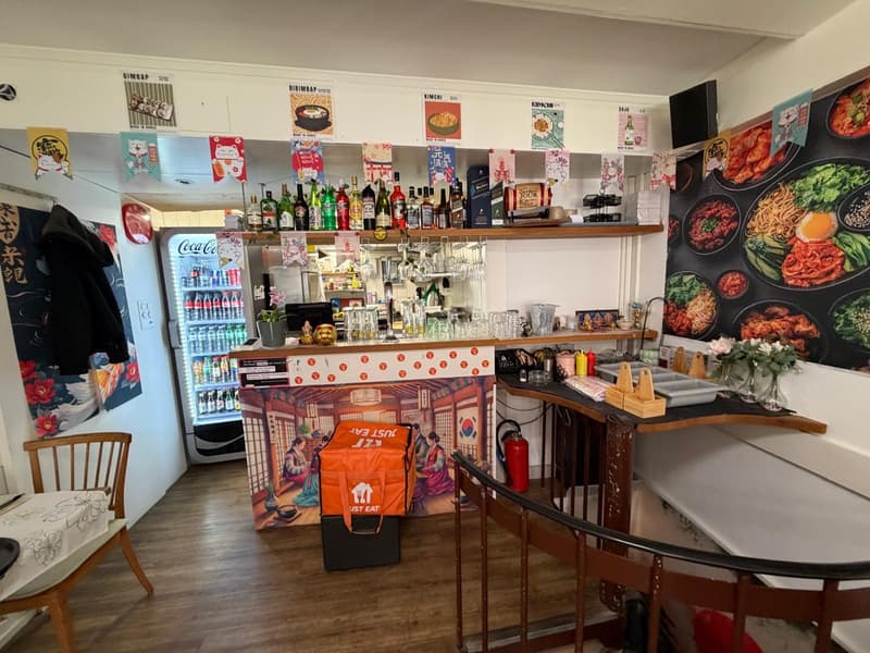 Counter with bottles, glasses, and food, a refrigerator with drinks, a chair, a table, a fire extinguisher, and a bag