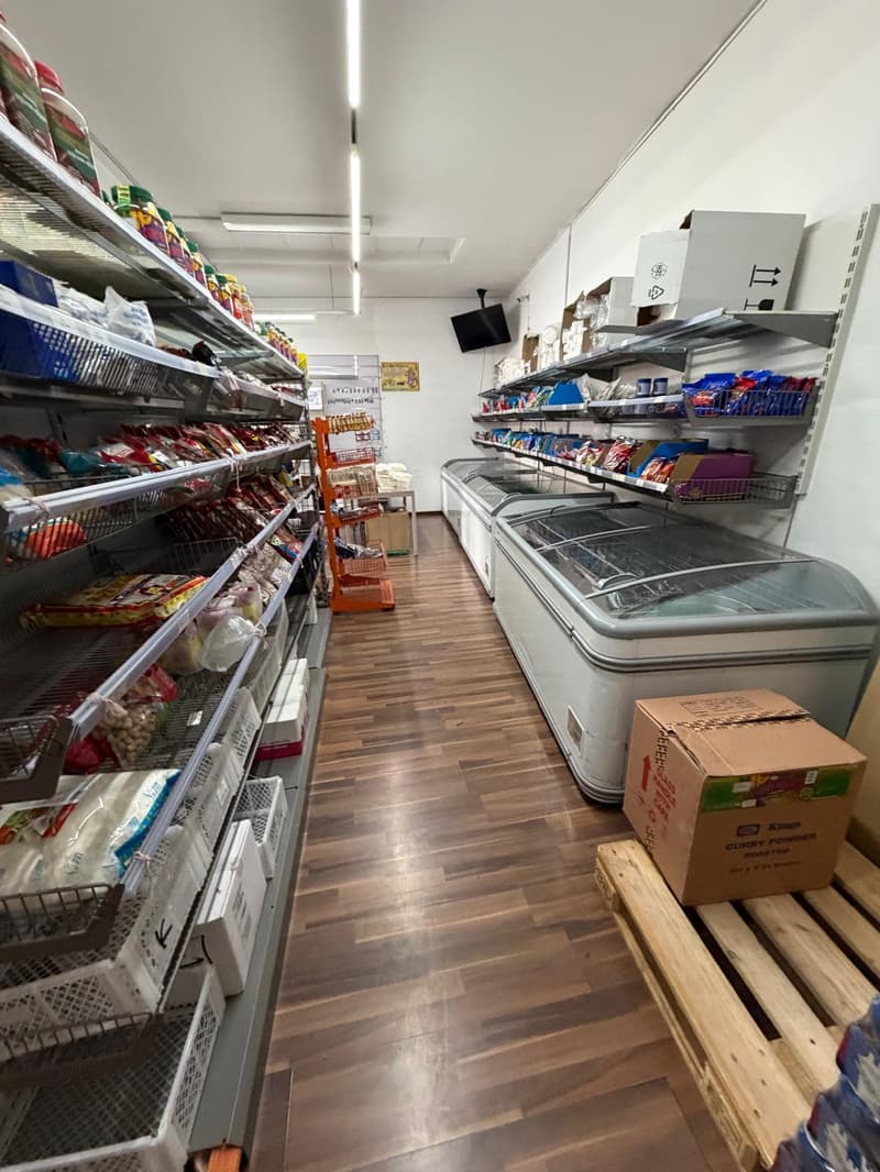 Store with wooden floor, shelves with products, freezers, storage boxes, and a monitor on the wall