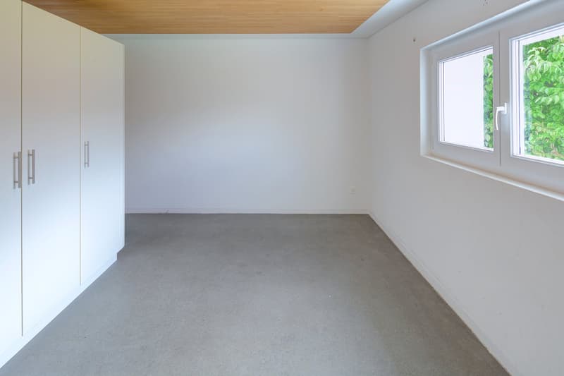 an empty room with white walls, gray floor, a window and white cabinets.