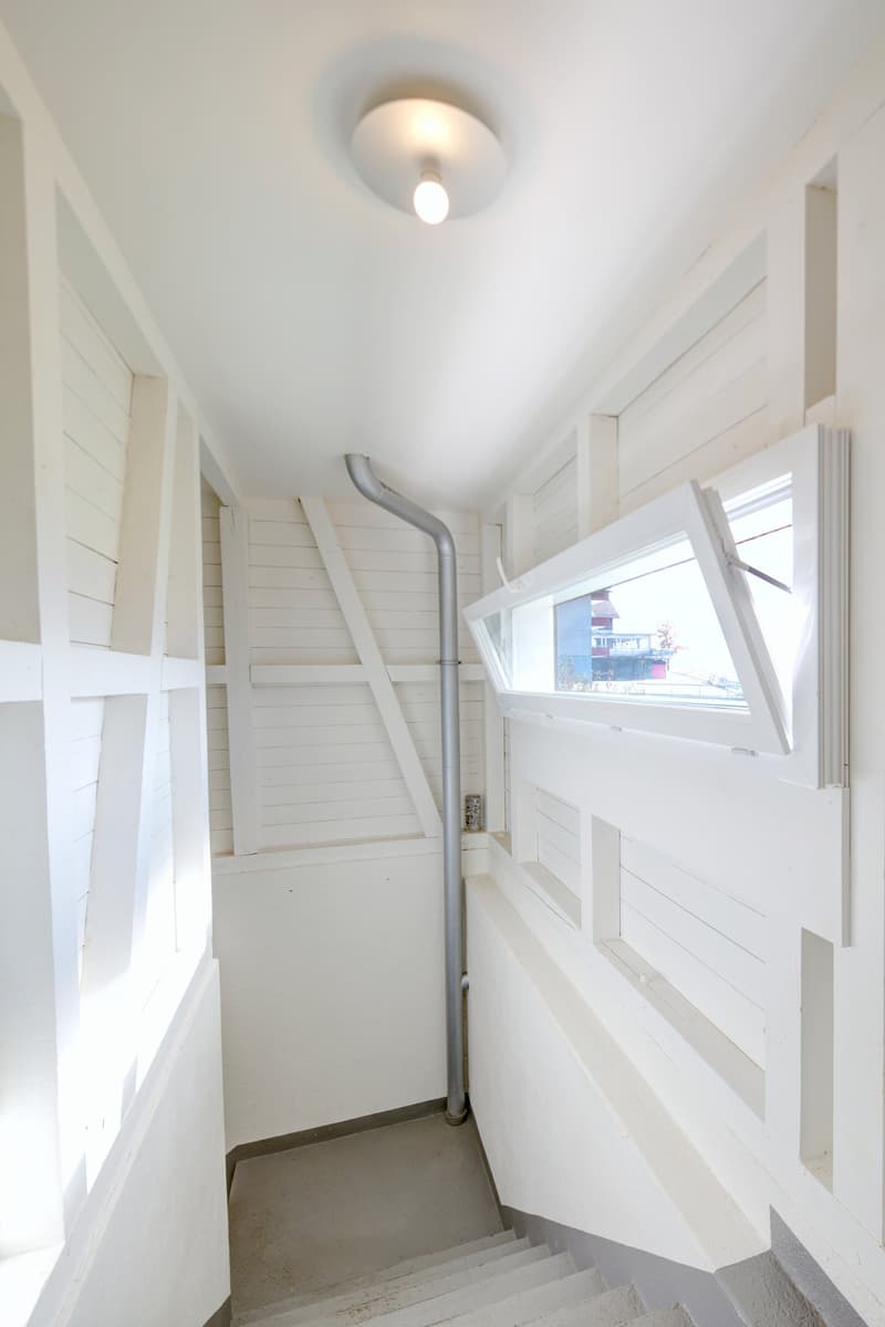 stairs leading down, white walls, wooden beams, open window, natural light, metal pipe