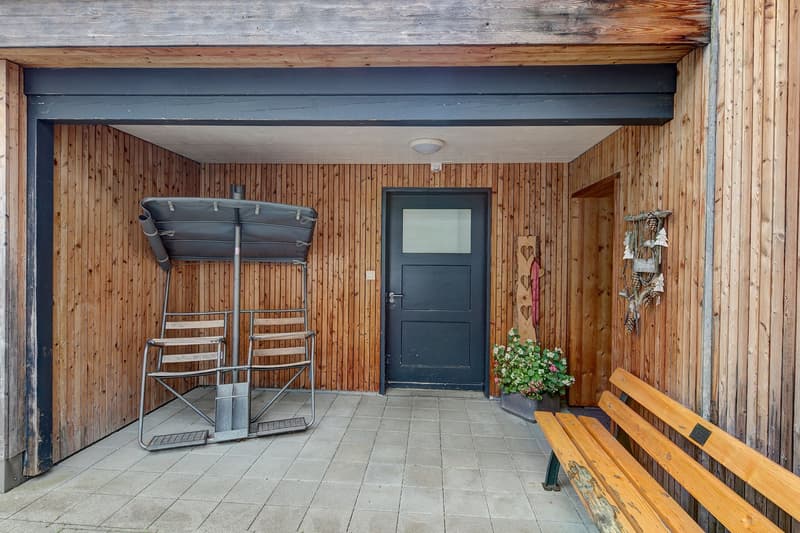 wooden walls, two outdoor chairs, metal railing, bench, potted plants, black door
