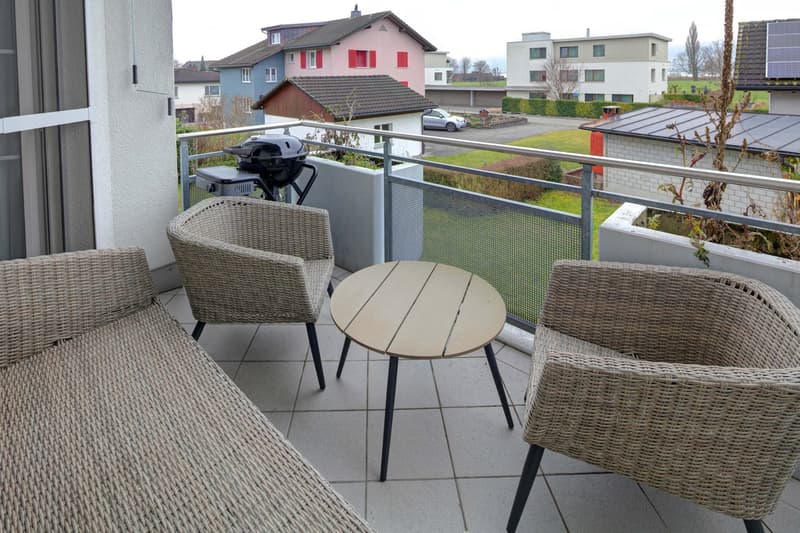 covered balcony with wicker furniture, BBQ grill, table, and a panoramic view of a parking lot and houses