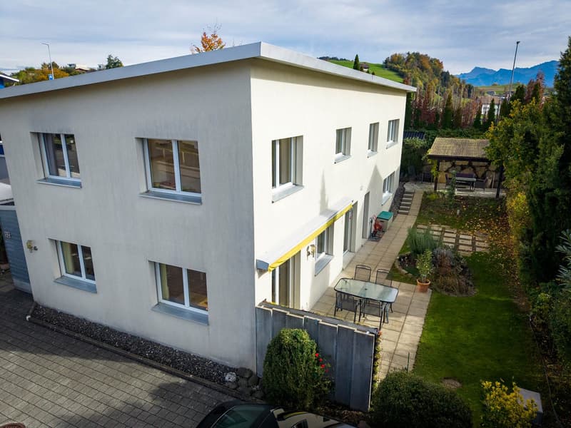 Detached house, 3 stories, white paint, large windows, balcony, yard with grass and plants, outdoor table and chairs, small garden