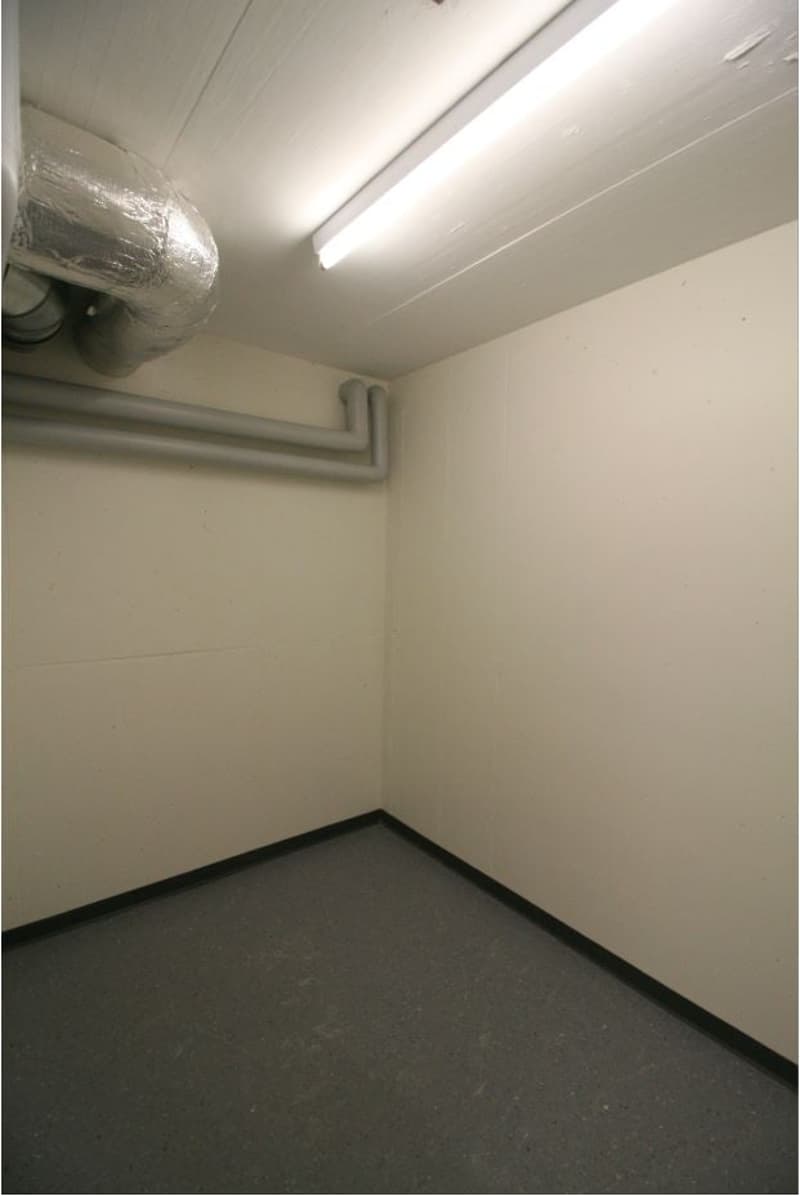 empty room with white walls, gray floor, pipes on the wall, a single light on the ceiling