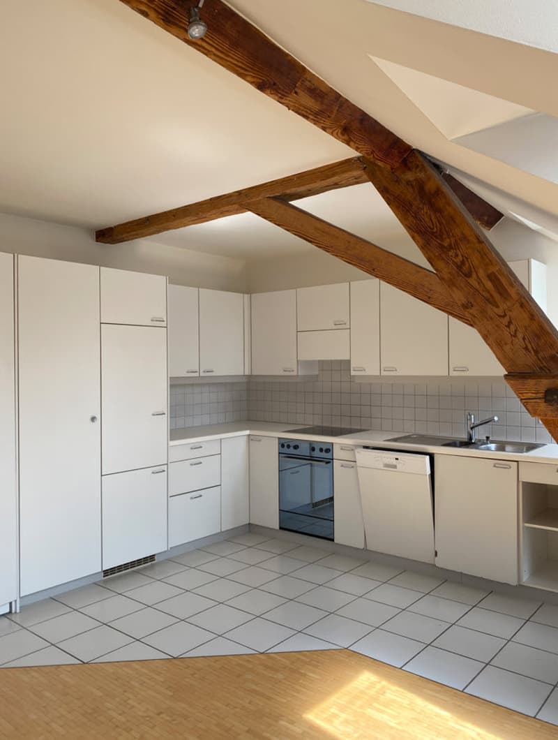 Spacious kitchen with white cabinets, tiled backsplash, and exposed wooden beams on the ceiling. The kitchen includes a dishwasher and other appliances.