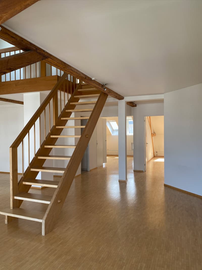 Open-plan living space with wooden staircase, hardwood flooring, and white walls
