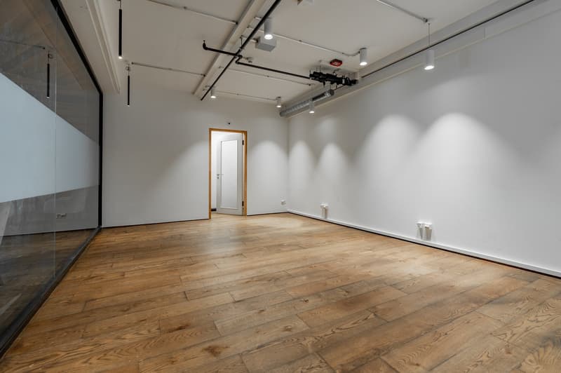 spacious room, white walls, wooden floor, suspended lights, glass partition, white door