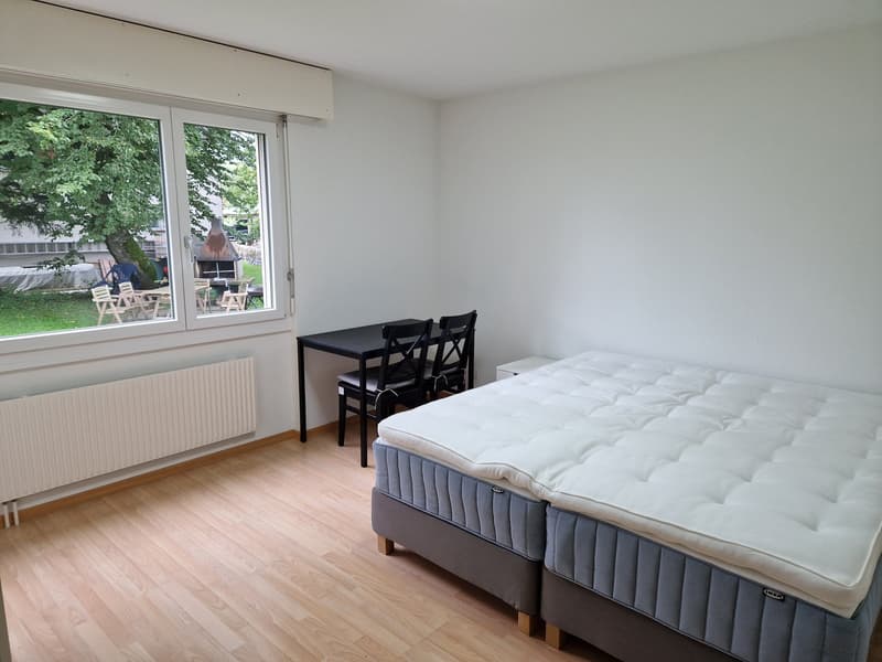 double bed, desk with 4 chairs, white radiator, large window with outdoor view