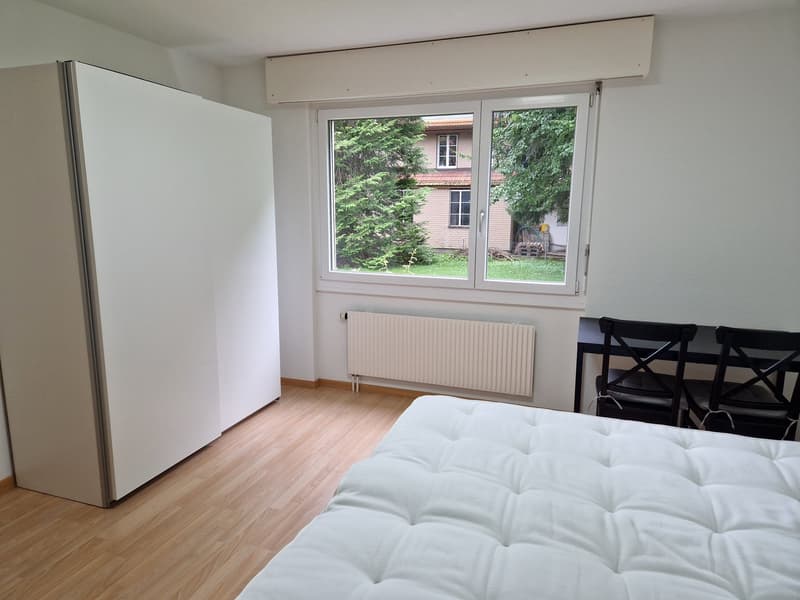bedroom with wooden floor, white bed, white wardrobe, radiator, and desk with two chairs