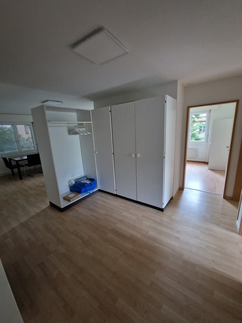 Empty room with white cupboards, wooden floor, small table with chairs, and a blue bag on the floor.