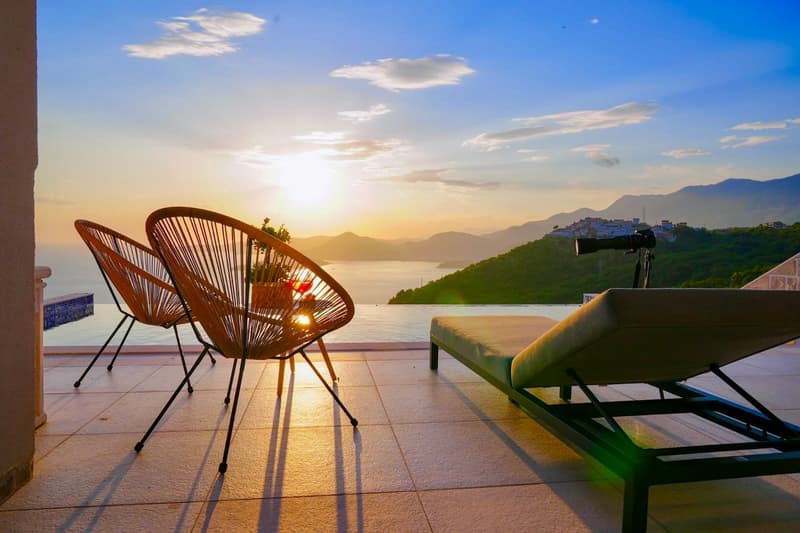 Terrace with lounge chair, outdoor chairs, and scenic view of ocean and mountains.