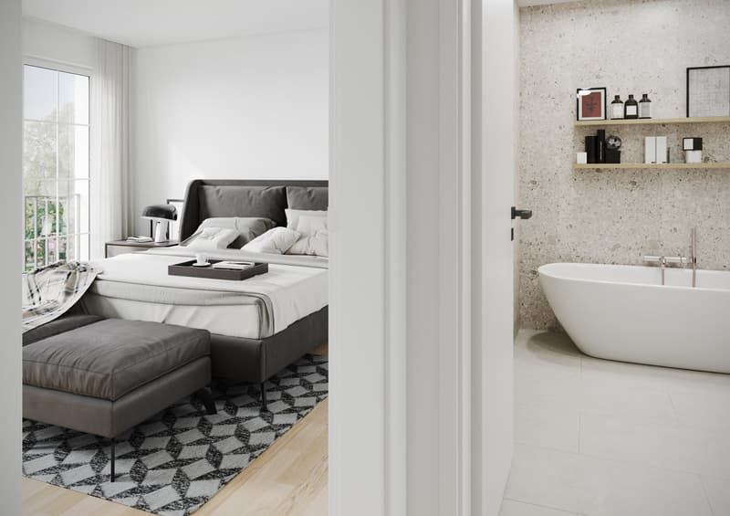 The image shows a modern bedroom with a large bed and gray upholstered furniture. The room has large windows and a balcony or terrace. There is also a bathroom visible, with a freestanding bathtub and shelves displaying various bathroom accessories. The o