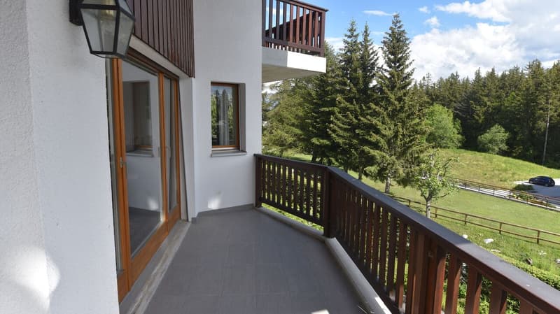 2-story house with a balcony overlooking a forested area, wooden railings, large windows, and a tiled floor on the balcony.