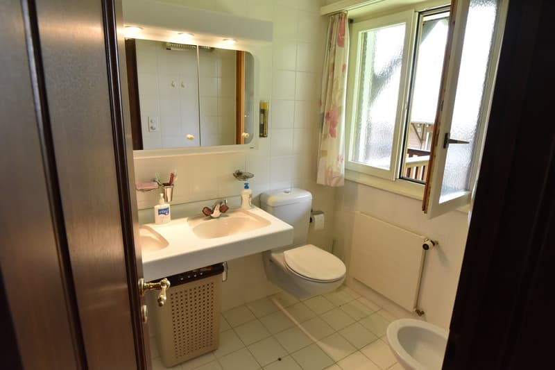 Bathroom with white tiles, vanity sink, mirror cabinet, toilet, and window