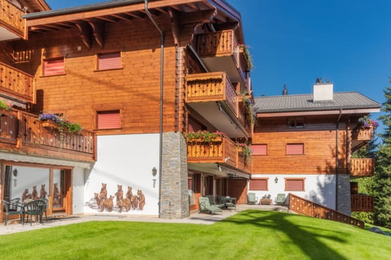 3-story wooden chalet-style apartment building with balconies, stone accents, and a grassy courtyard area