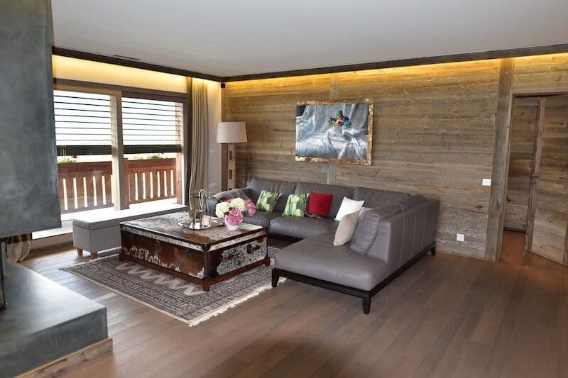 Spacious living room with wooden walls, large windows, gray sectional sofa, wooden coffee table, and artwork on the wall.