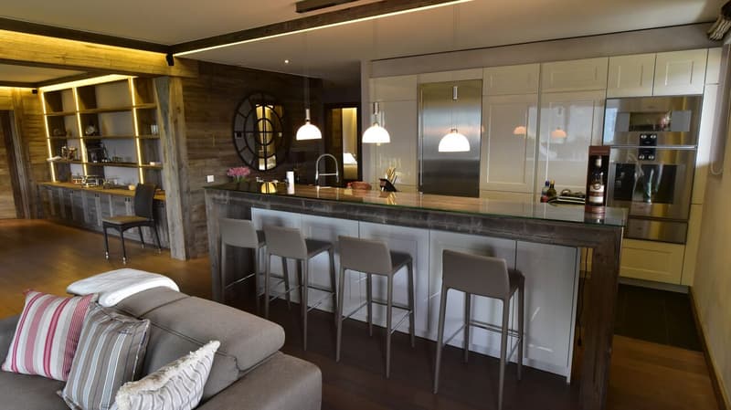 Open-concept kitchen and living room with rustic wood accents, modern appliances including a dishwasher, a large kitchen island with bar seating, and a fireplace in the living area.