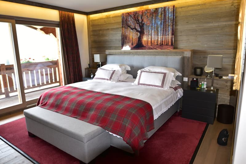 Cozy bedroom with wooden walls, large bed with plaid blanket, nightstands, and a balcony with a scenic view