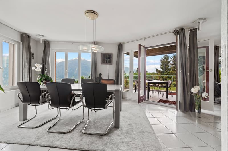 Spacious dining room with large windows offering a scenic mountain view, modern dining table and chairs, pendant lighting fixture, and sliding glass doors leading to a balcony or terrace