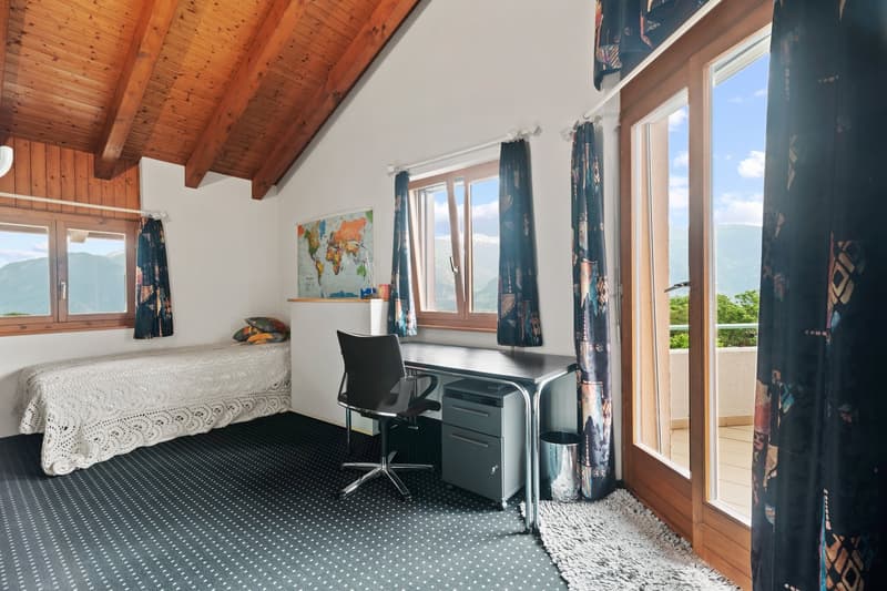 Attic bedroom with wooden ceiling, large windows, desk, chair, bed, and world map on the wall