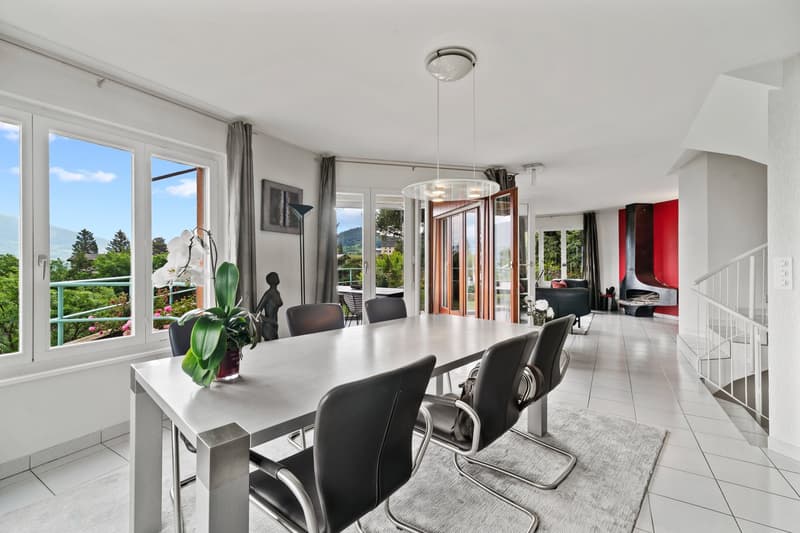 Open-concept living and dining area with large windows offering a scenic view, modern dining table and chairs, pendant lighting fixture, and access to a balcony or terrace