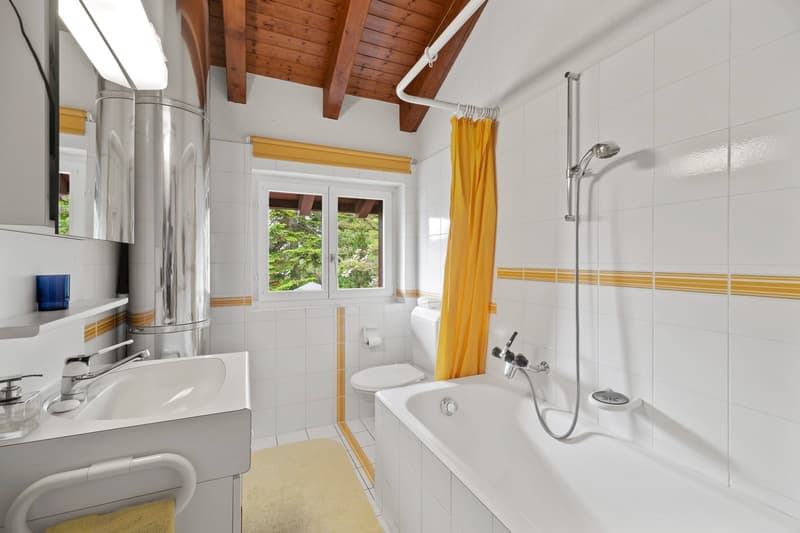 Bathroom with white tiled walls, wooden ceiling beams, large window, bathtub, vanity sink, and yellow shower curtain