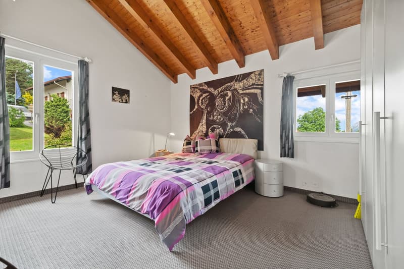 Spacious bedroom with wooden beamed ceiling, large windows overlooking the garden, plaid bedding, and a decorative wall art piece above the bed.