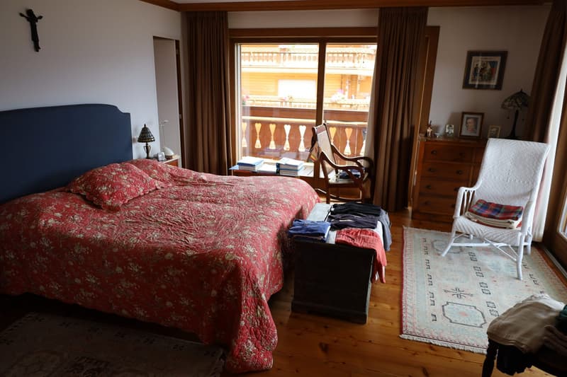 Large bedroom with a king-size bed, wooden furniture, and a balcony overlooking the exterior. The room has hardwood floors, curtains, and various decor items.