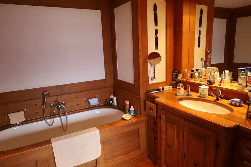 Spacious bathroom with wooden walls and vanity, large bathtub, and various toiletries and personal care items on the vanity.