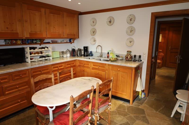 Spacious kitchen with wooden cabinets, marble countertops, sink, dishwasher, and various kitchen appliances. The kitchen also features a dining table with wooden chairs and decorative plates on the wall.