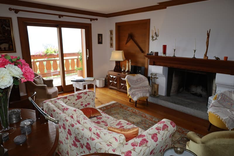 Cozy living room with floral patterned sofa, wooden furniture, fireplace, and access to a balcony or terrace through large windows