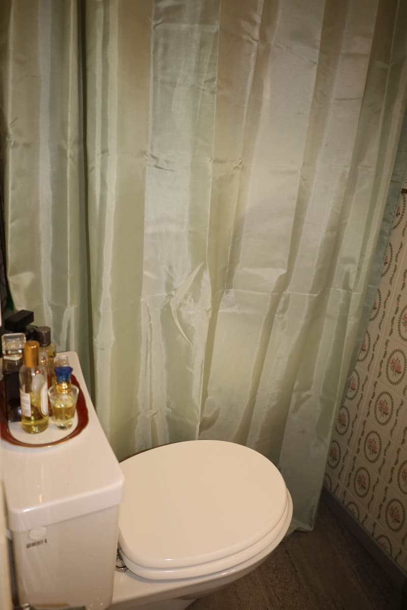 White toilet, tray with toiletries, white shower curtain, floral wallpaper