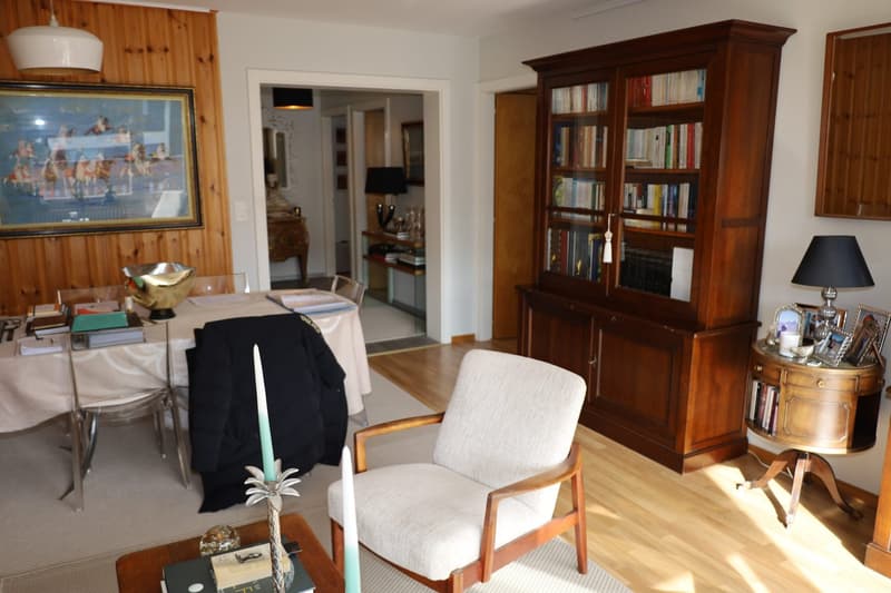 Dining area with table and chairs, bookcase, armchair, lamp, rug