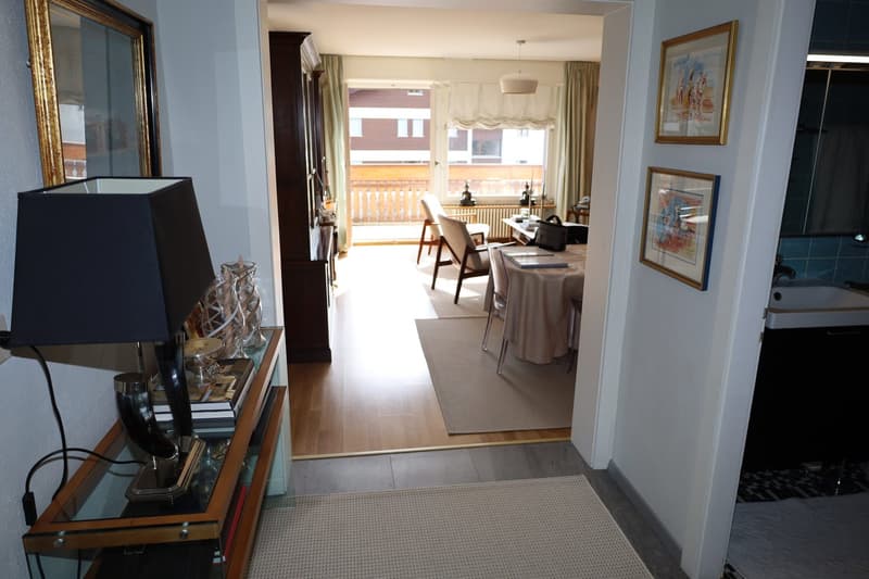 interior hallway, wooden flooring, dining table with chairs, rug, balcony, radiator, desk, shelves with books, lamp, frames, mirror