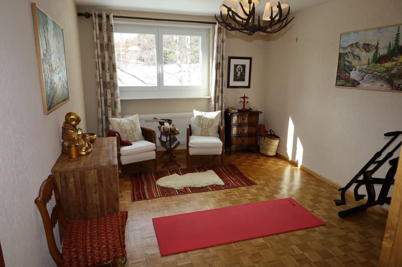 Wooden floor, two white armchairs, rug, yoga mat, wooden cabinet, small table, pictures on the wall, fireplace
