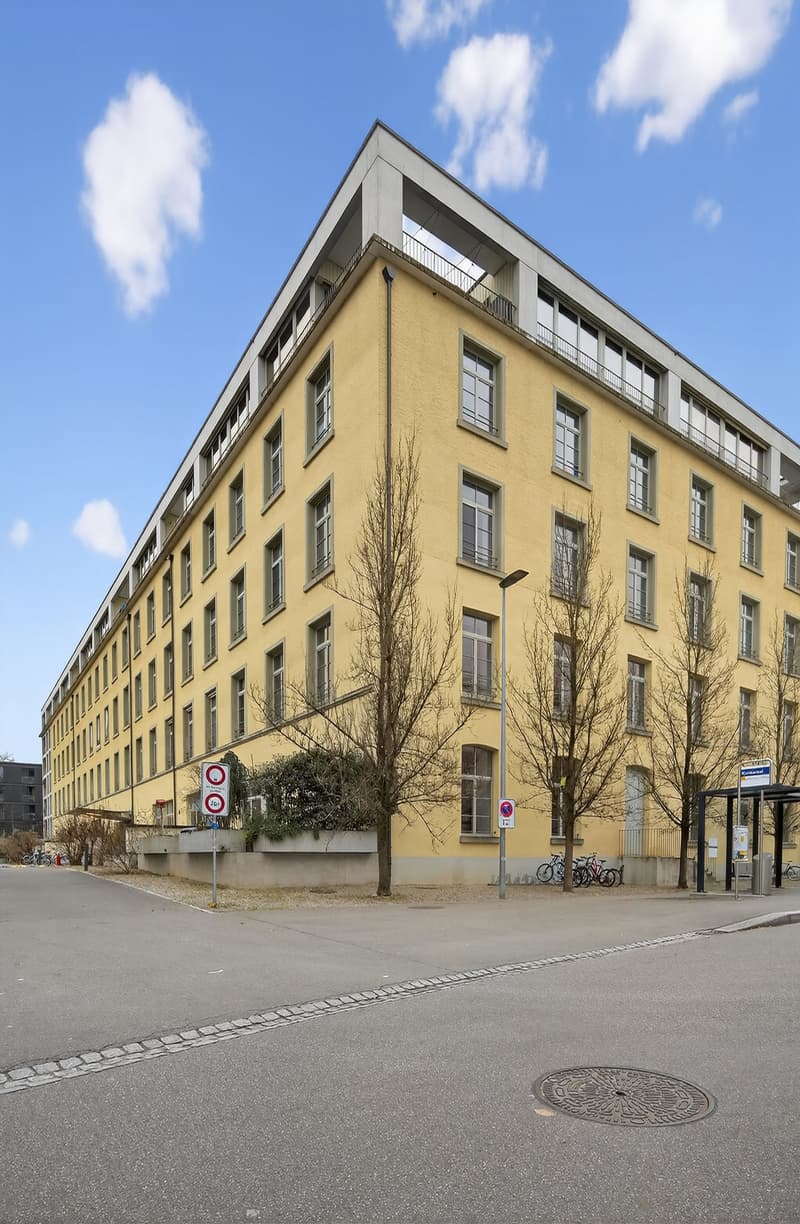 A yellow apartment building with multiple floors and numerous windows, with bicycle stands on the left side and bicycles parked.