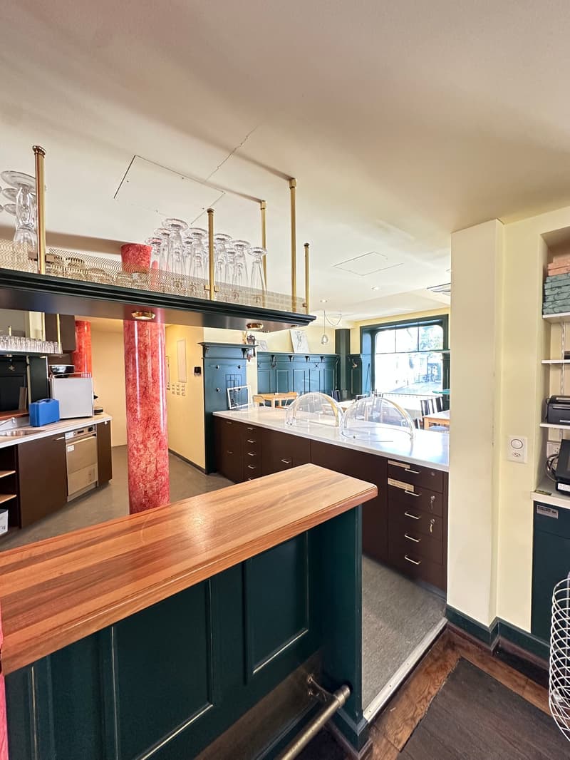 bar area, wooden counter, marble column, wine glasses on shelf, green cabinets, counter with drawers, power outlet, white ceiling