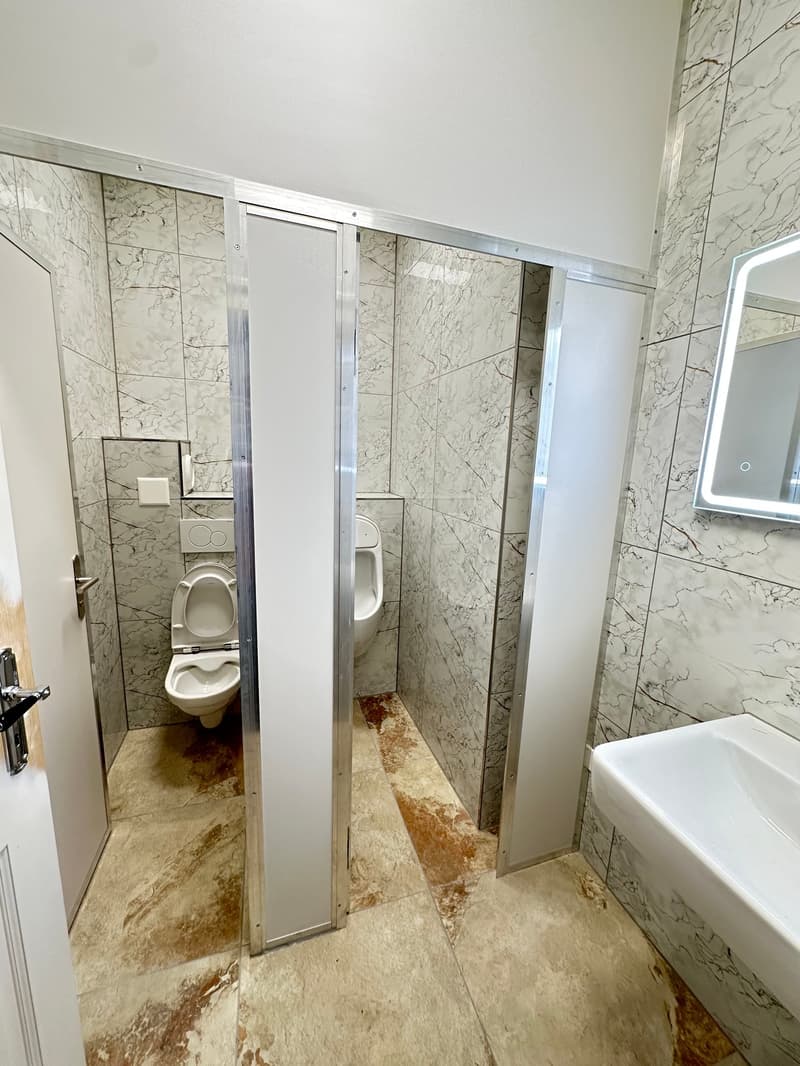 marble tiled walls, modern toilet cubicles, single urinal, vanity sink