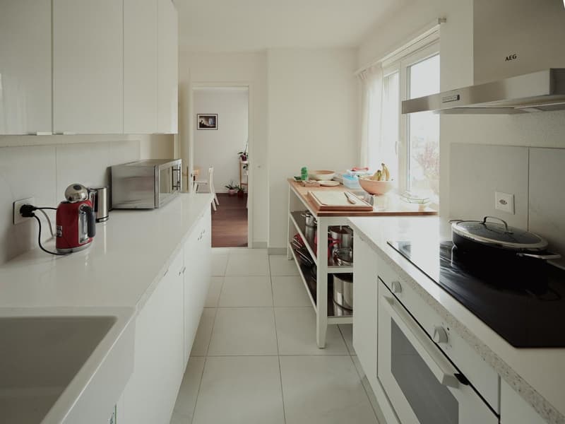 modern kitchen, white tiled flooring, white cabinetry, electric stove, oven, microwave, dishwasher, open shelves, wooden table, sink, kettle, countertop with food, extractor fan, power outlets