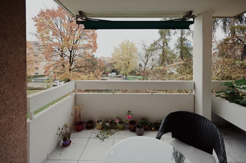 white tiled floor, table, black wicker chair, various potted plants, white railings, outdoor view