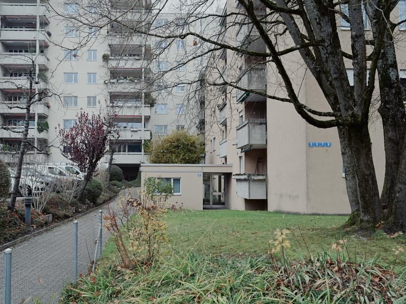 A multi-story residential building with balconies and a fenced yard.