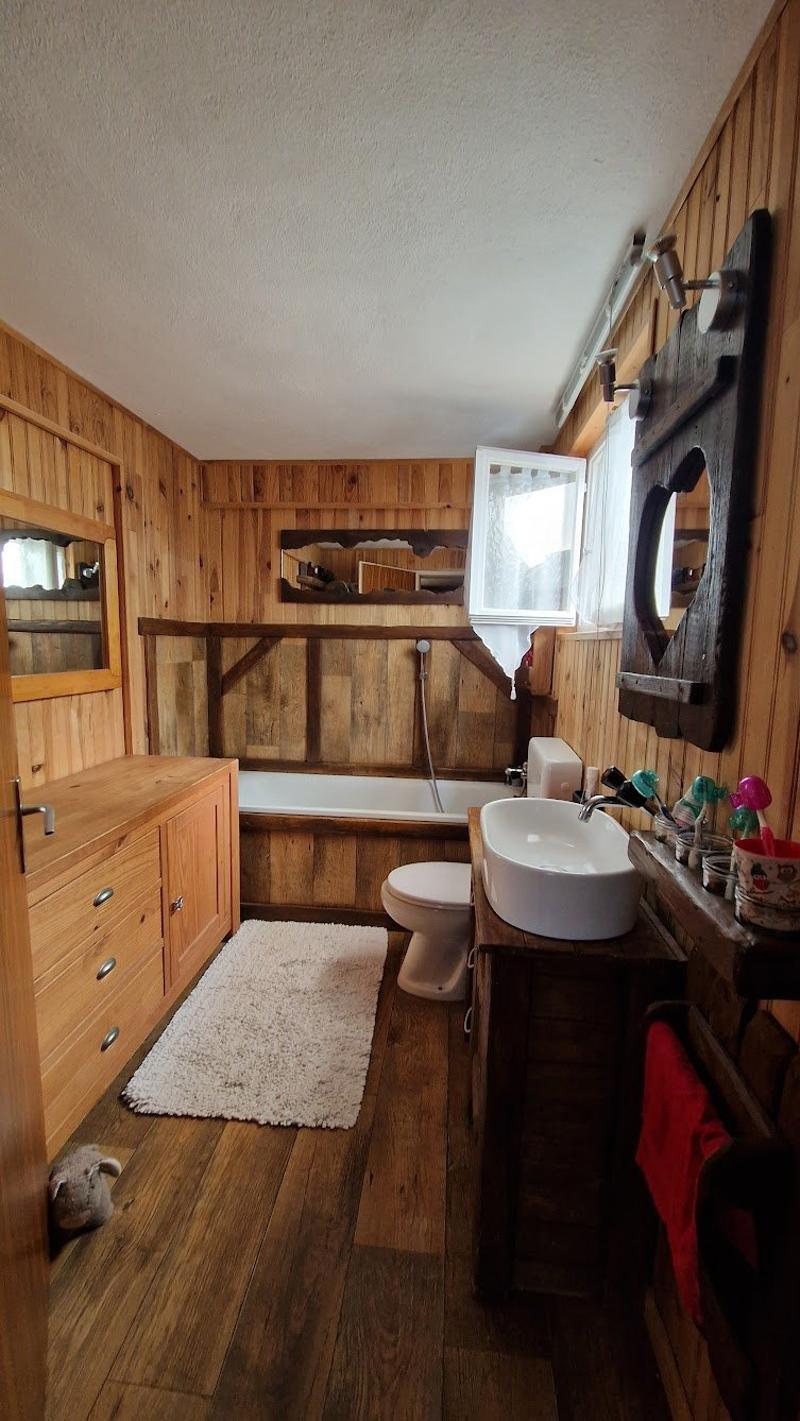 Rustic bathroom with wooden walls and floors, a bathtub, a vanity with a sink, and a toilet. There is also a cabinet and some decor items visible.