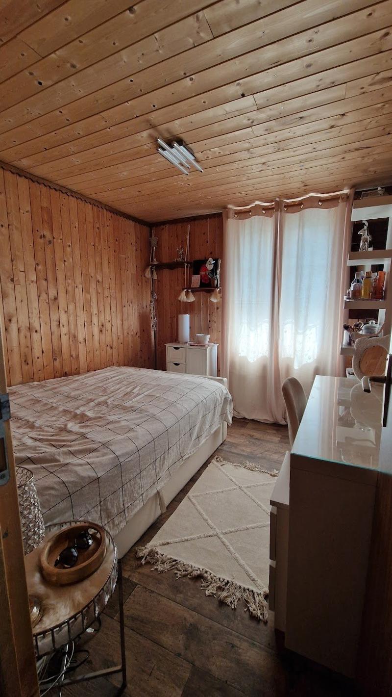 Cozy bedroom with wooden walls and ceiling, a bed with a patterned comforter, shelves and storage units, and a fireplace visible in the corner.