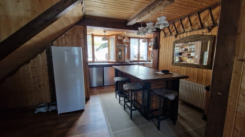 Rustic wooden interior with exposed beams, kitchen island with stools, stainless steel refrigerator, and hanging light fixtures