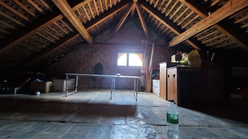 Wooden beams and trusses in the attic, with a table and some storage items visible. The space appears to be used for storage or as a workspace.