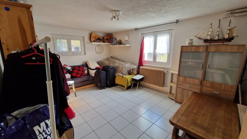 a couch with two pillows, a guitar on the shelf, a bag with the letters my, a wooden table, a cabinet with glass doors, a radiator, and a stool