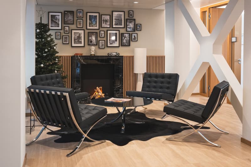 fireplace, four black leather armchairs, round table with magazine, black rug, Christmas tree, photo frames, wooden pillar