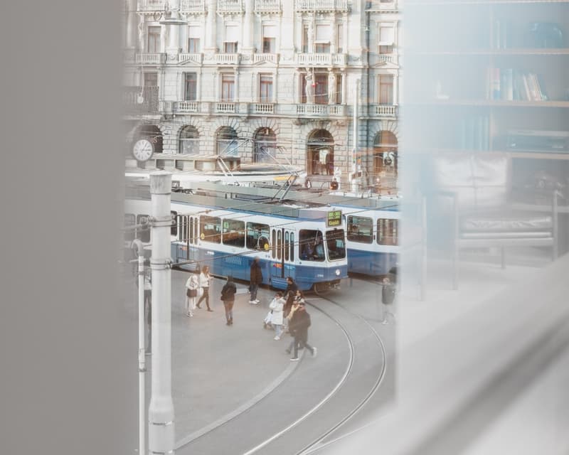 Outdoor view of a busy street with trams and people walking, large building in the background